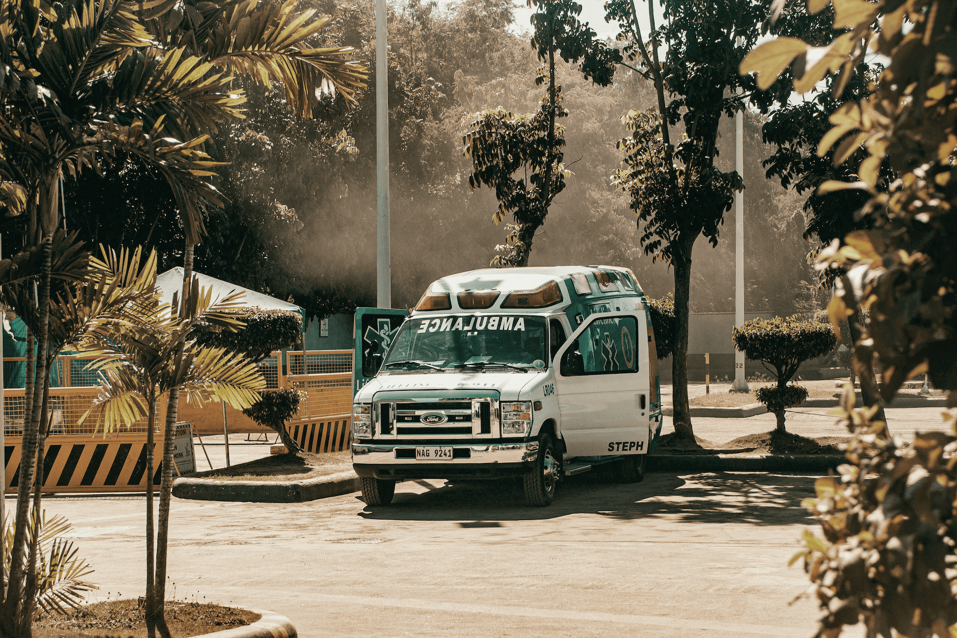 White ambulance parked in a sunny lot surrounded by trees with a golden-brown filter.