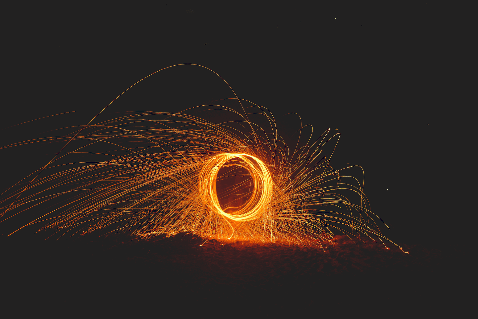 Long exposure light painting showing a bright ring of golden sparks with trails spraying outward against a dark background.