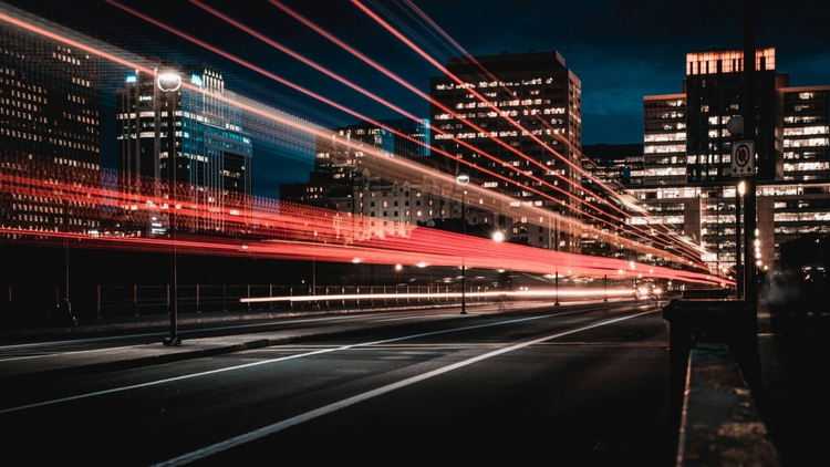 Night cityscape with light trails from fast-moving cars symbolizing digital transformation, data flow, and AI-powered smart city technology by Neoteric.
