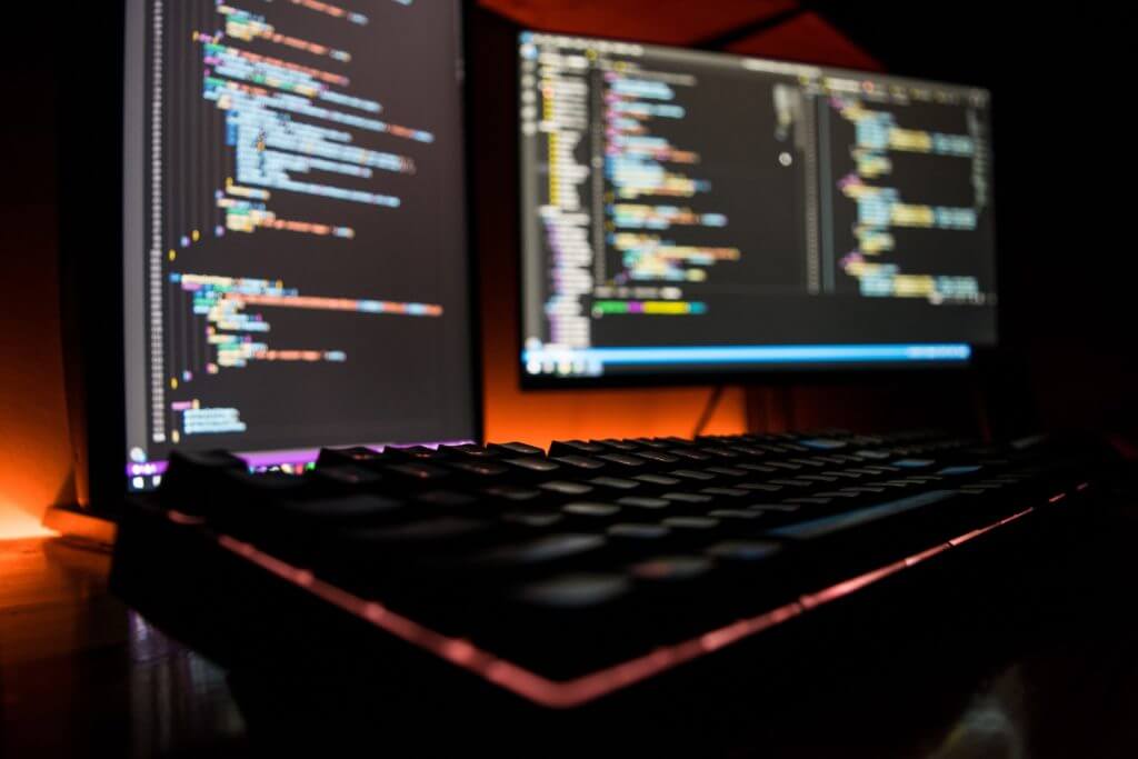 Computer screens displaying code, illustrating the difference between Node.js and React in web development.