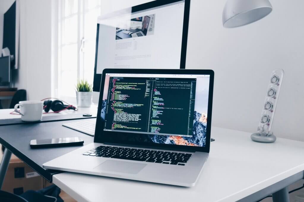 Laptop displaying code on a clean wite desk symbolizing bespoke software development company.