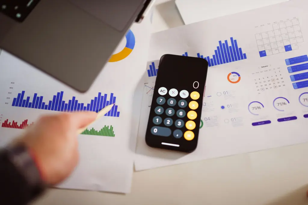 AI Development budget planning with a calculator, laptop, financial charts, and project performance data